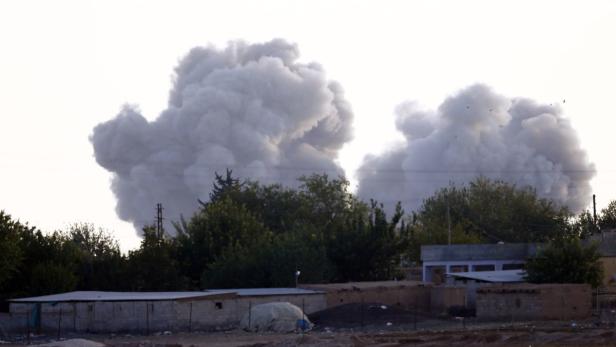 Über Bäumen und Gebäuden steigt dichter Rauch auf.