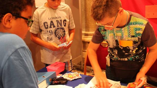 Drei Jungen stehen an einem Tisch und sortieren Spielkarten.