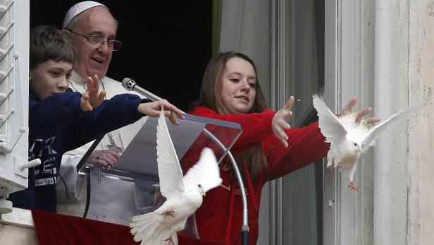 Papst Franziskus lässt mit zwei Kindern weiße Tauben vom Fenster aus fliegen.