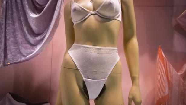 Eine Schaufensterpuppe trägt weiße Spitzenunterwäsche vor einem rosa Hintergrund.