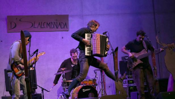 Die Band D’Slalombríada tritt mit Akkordeon, Gitarre, Bass und Schlagzeug auf einer Bühne auf.