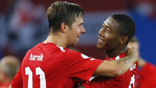 Zwei Fußballspieler in roten Trikots umarmen sich auf dem Spielfeld.