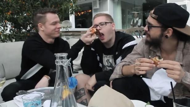 Drei Männer sitzen an einem Tisch im Freien und essen Pizza.