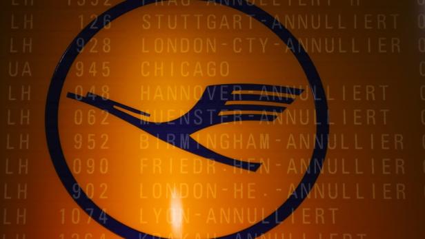 Das Lufthansa-Logo vor einer Anzeigetafel mit annullierten Flügen.