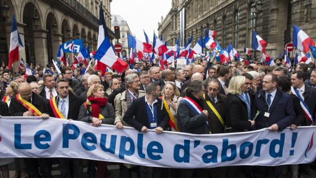 Eine Menschenmenge demonstriert mit französischen Flaggen und einem Banner mit der Aufschrift „Le Peuple d'abord!“.