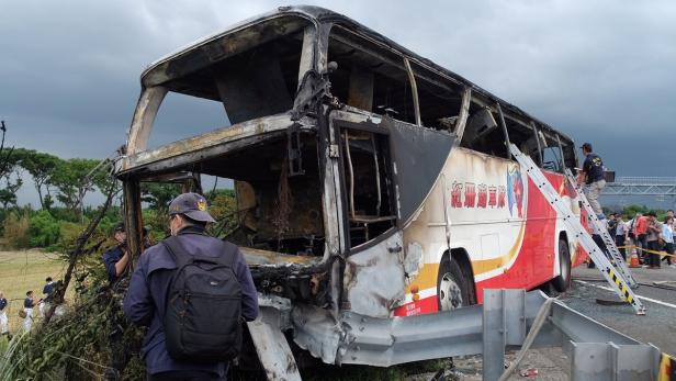 Ein ausgebrannter Bus steht am Straßenrand, während Ermittler die Szene untersuchen.