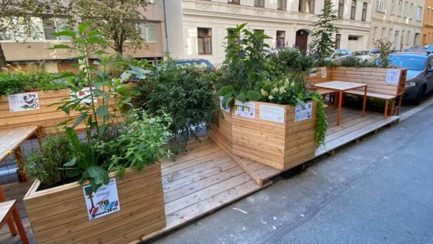 Eine begrünte Parklet-Installation mit Holzbänken und Pflanzkästen am Straßenrand.