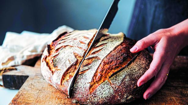 Woman cutting sourdough bread with knife on board