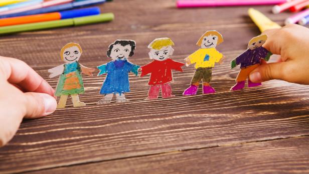 the child does figures of people of paper. Paper people on wooden background. Creative child play with craft.