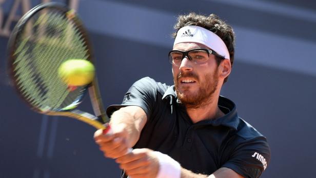 Ein Tennisspieler mit Brille und Stirnband schlägt einen Tennisball.