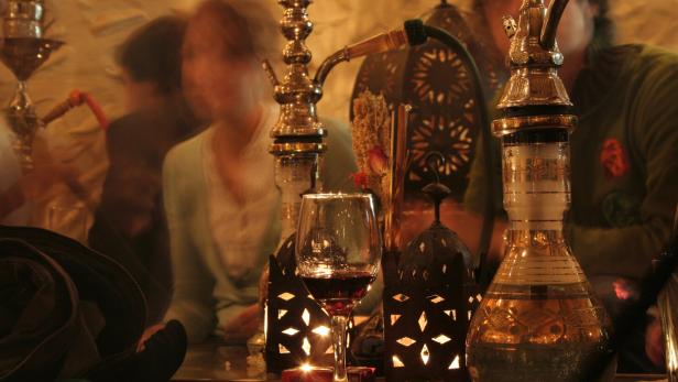 Hookah pipes next to glass of red wine and lanterns