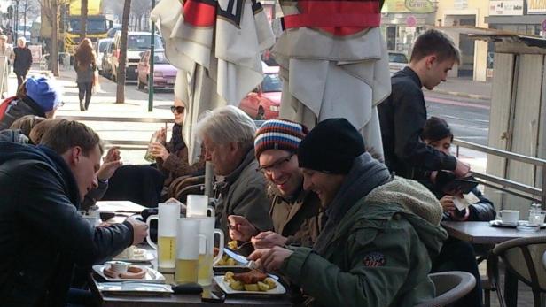 Eine Gruppe von Menschen sitzt an einem Tisch im Freien und isst zu Mittag.