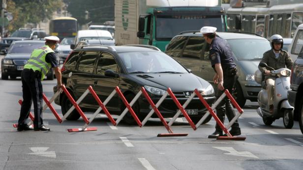Polizisten sperren eine Straße mit rot-weißen Absperrgittern ab.