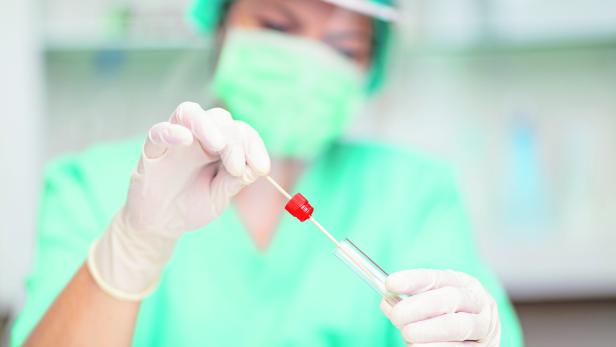 Healthcare worker in protective workwear putting swab stick into test tube