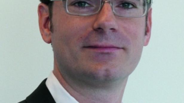 Ein Mann mit Brille und dunklem Anzug blickt in die Kamera.