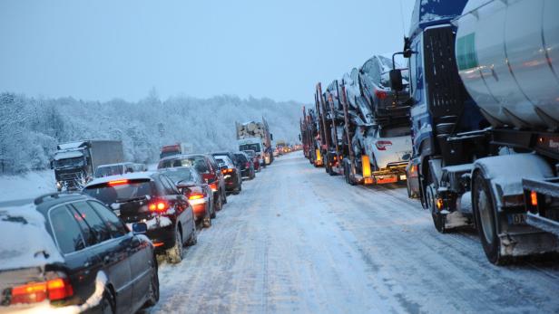 Auf einer verschneiten Straße staut sich der Verkehr mit Autos und Lastwagen.