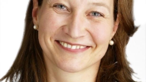 Eine lächelnde Frau mit braunen Haaren und einem schwarzen Blazer.