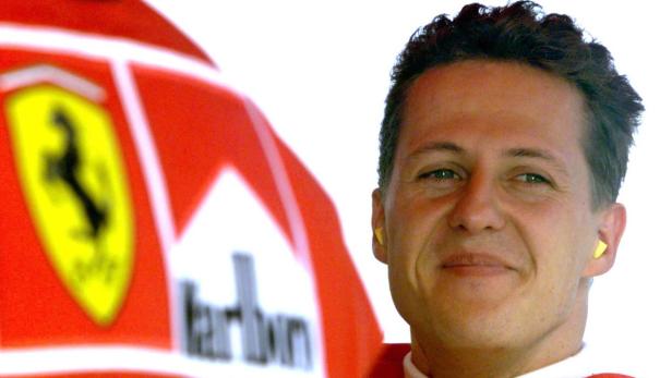 Michael Schumacher mit Ohrstöpseln vor einer Ferrari-Flagge.