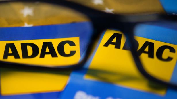 Gelbe ADAC-Aufkleber liegen auf einem blauen Untergrund, teilweise durch eine Brille betrachtet.