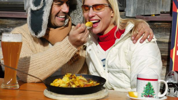 Ein Paar isst Bratkartoffeln und trinkt Bier in einer Skihütte.