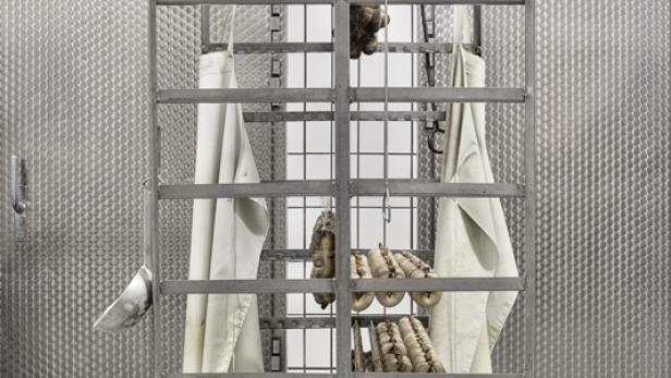 Ein fahrbares Gestell mit Wurstwaren und weißen Schürzen in einem Kühlraum.