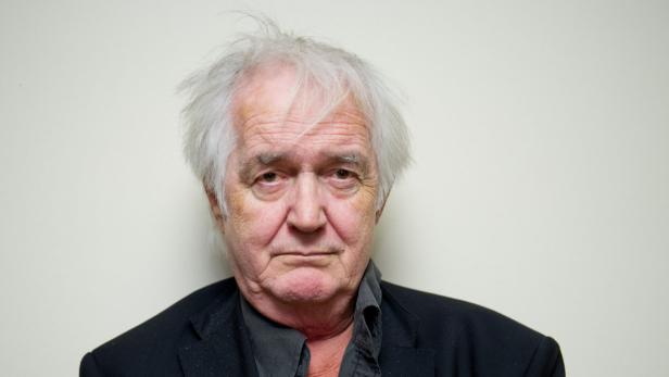 Porträt eines älteren Mannes mit grauem Haar und dunklem Anzug vor einem hellen Hintergrund.