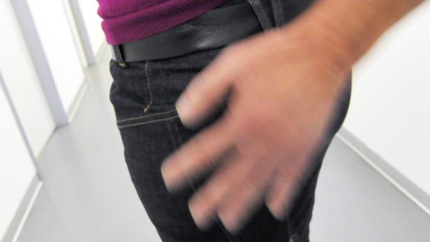 Eine Person in Jeans und einem lila Oberteil mit einer Hand in der Hosentasche.