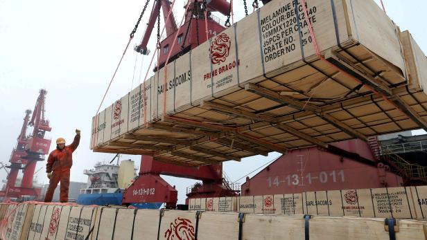 Worker gestures as a crane lifts goods for export onto a cargo vessel at a port in Lianyungang, Jiangsu