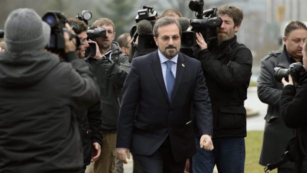 Ein Mann in einem Anzug wird von einer Gruppe von Reportern und Kameraleuten umringt.