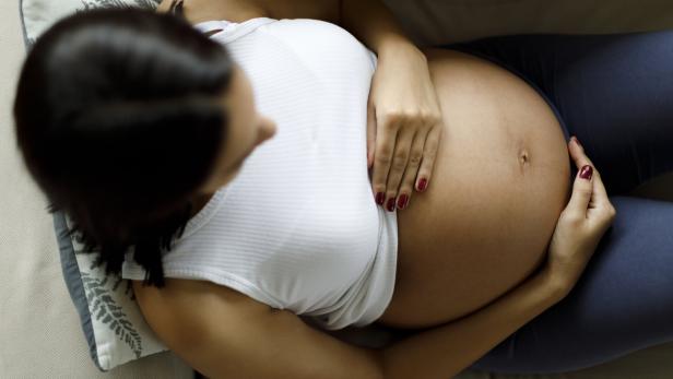 Eine schwangere Frau greift sich auf den Bauch.