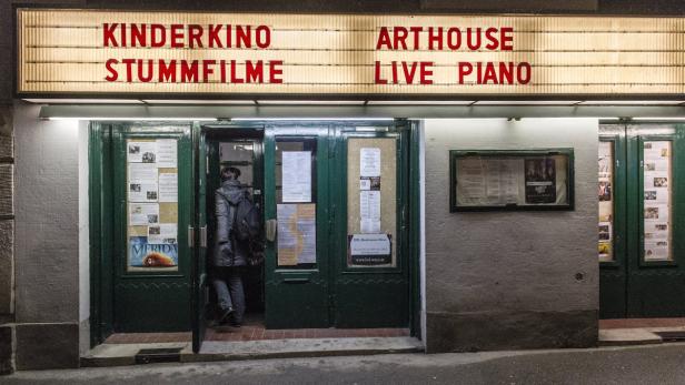 Eine Person betritt ein Kino, das „Kinderkino Stummfilme“ und „Arthouse Live Piano“ zeigt.