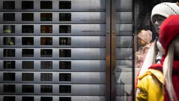 Zwei Schaufensterpuppen mit Winterkleidung stehen hinter einem teilweise geschlossenen Metallrolltor.