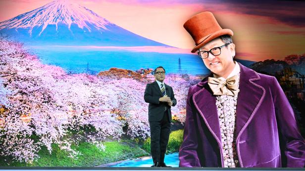 Ein Mann im Anzug steht vor einer Projektion des Fuji mit blühenden Kirschbäumen.