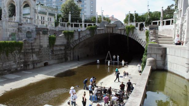 Ein Filmteam dreht eine Szene in einem Kanal unter einer Brücke.