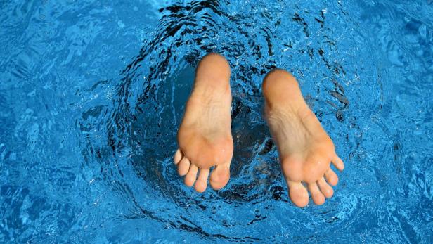Zwei Füße ragen aus dem blauen Wasser.