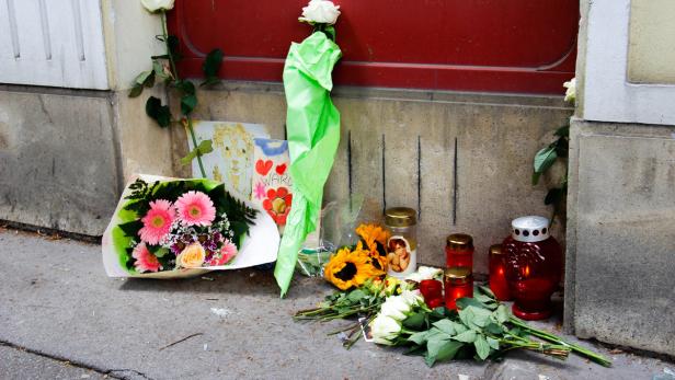 Blumen, Kerzen und Kinderzeichnungen liegen vor einer roten Tür.