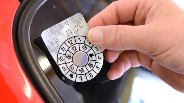 Eine Hand klebt eine österreichische Prüfplakette an eine Windschutzscheibe.