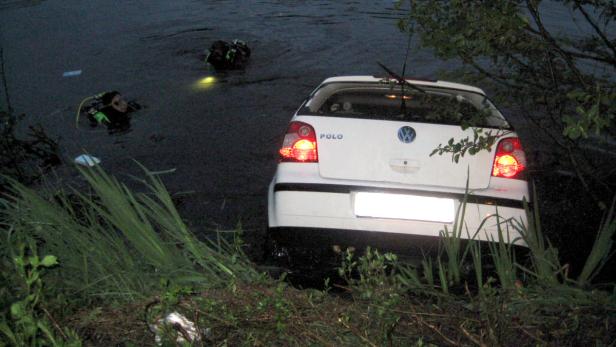 Ein weißer VW Polo steht im Wasser, während Taucher im Hintergrund zu sehen sind.