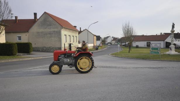 Ein Mann fährt einen roten Traktor durch eine ländliche Gegend.