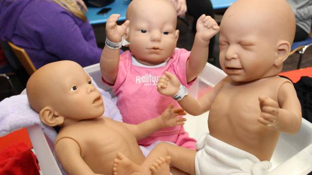 Drei Babypuppen liegen in einer Wanne, eine davon trägt ein rosa T-Shirt.