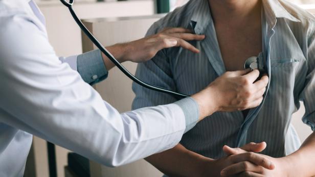 Arzt untersucht mit Stethoskop den Brustkorb eines sitzenden Patienten.