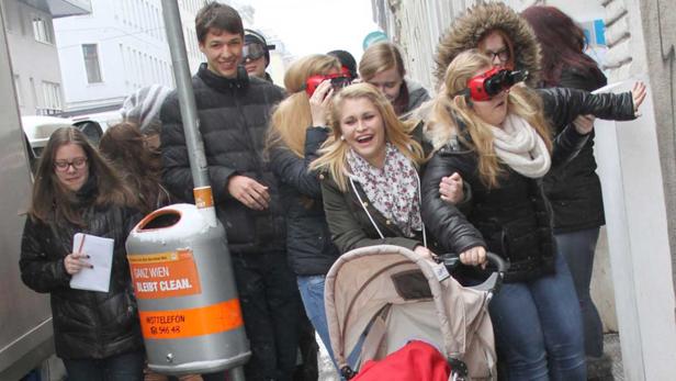 Eine Gruppe junger Leute, einige mit seltsamen Brillen, schiebt einen Kinderwagen auf der Straße.