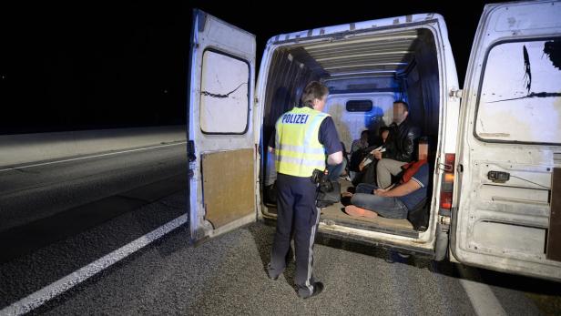 Ein Polizist kontrolliert eine Gruppe von Menschen in einem Lieferwagen bei Nacht.