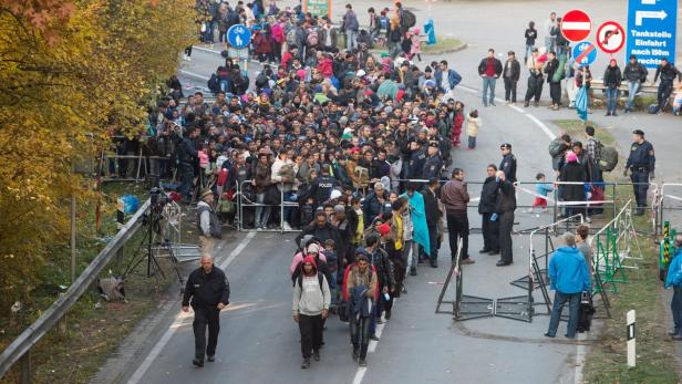 Flüchtlinge überqueren im Oktober 2015 nahe Passau neben Polizisten die deutsch-österreichische Grenze.