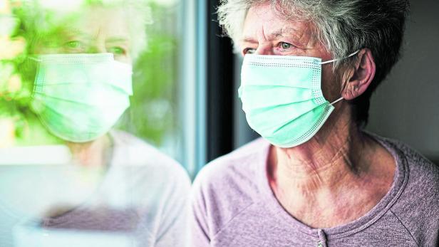 a old woman or grandma is wearing a respirator or surgical mask and looking out of the window