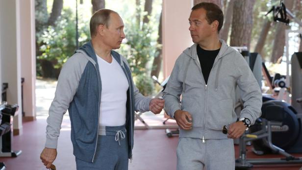 Wladimir Putin und Dmitri Medwedew unterhalten sich in Trainingsanzügen in einem Fitnessstudio.