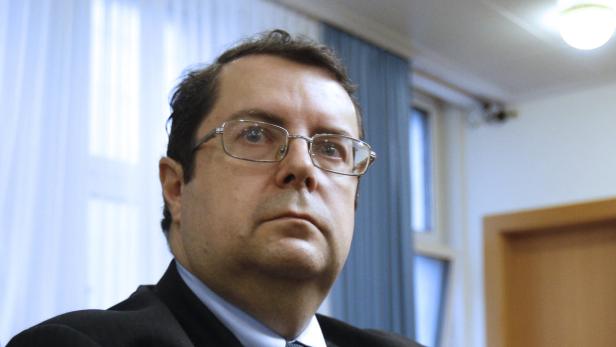 Ein Mann mit Brille und dunklem Anzug blickt aufmerksam nach oben.