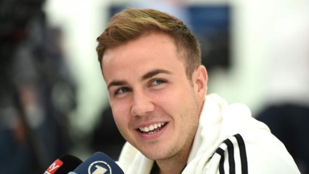 Mario Götze lächelt in die Kamera, während er von Mikrofonen umgeben ist.