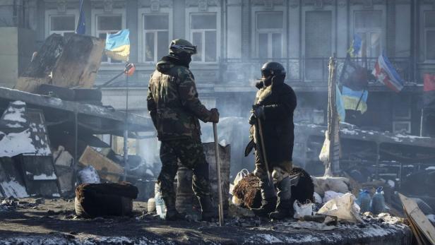 Zwei Personen stehen inmitten von Barrikaden und ukrainischen Flaggen.