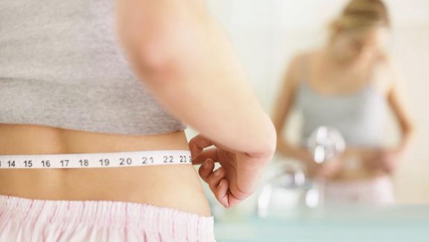 Eine Frau misst ihren Taillenumfang mit einem Maßband.